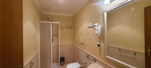 A bathroom with a toilet, a sink, a hairdryer mounted on the wall, and a shower area. - Sandel Giubileo Hotel (ROMA)