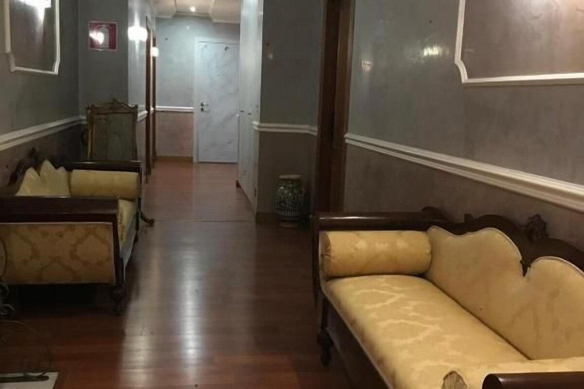 A hallway with a sofa, a chair, and a bed in the background.