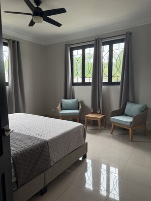 Un dormitorio con una cama, dos sillas, una mesita y un ventilador de techo.