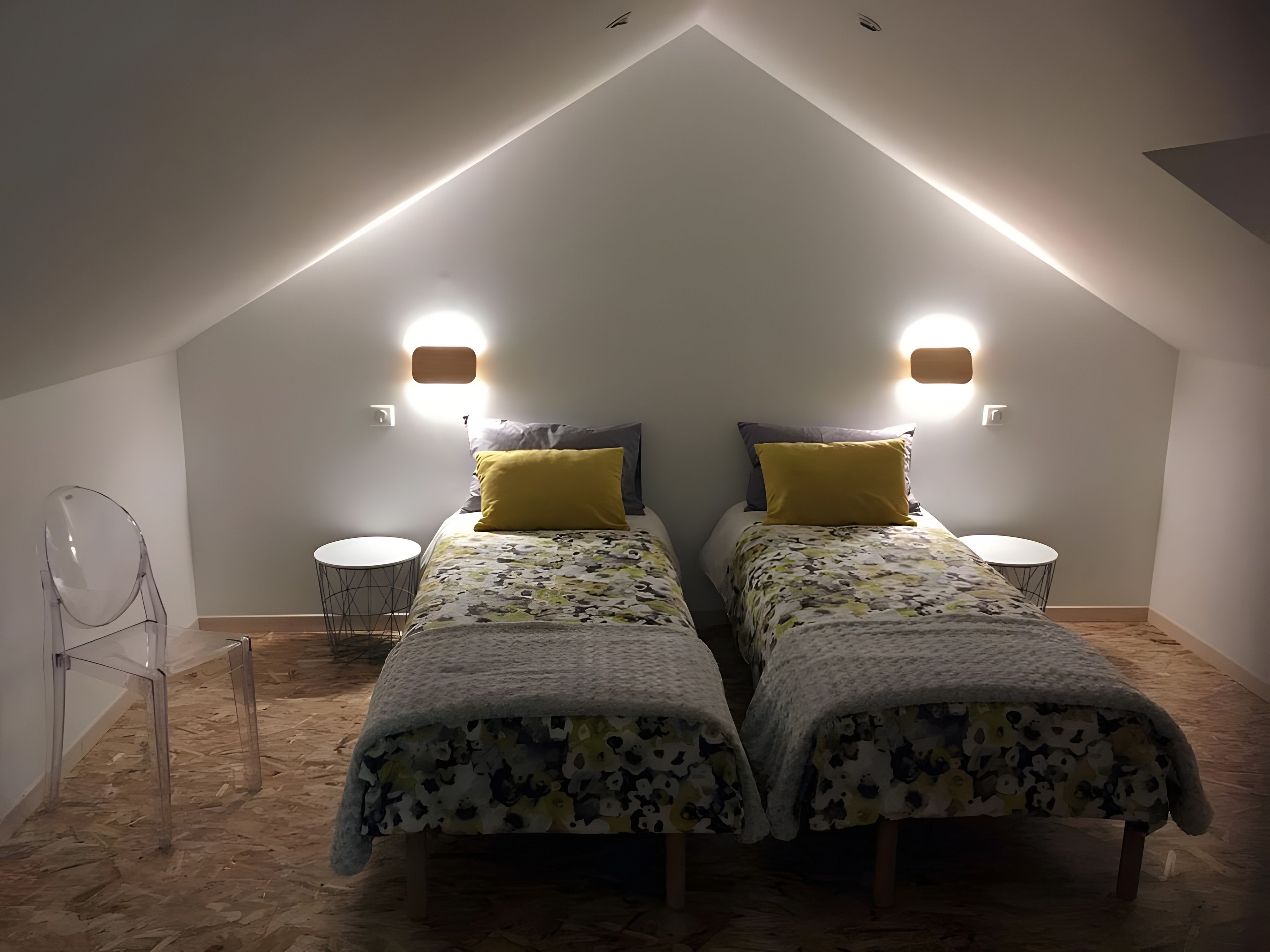 Une chambre avec deux lits, chacun recouvert d’une couvre-lit à motifs et agrémenté d’un seul oreiller jaune. Deux lampes murales sont fixées de part et d’autre des lits.