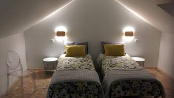 Une chambre avec deux lits, chacun recouvert d’une couvre-lit à motifs et agrémenté d’un seul oreiller jaune. Deux lampes murales sont fixées de part et d’autre des lits.