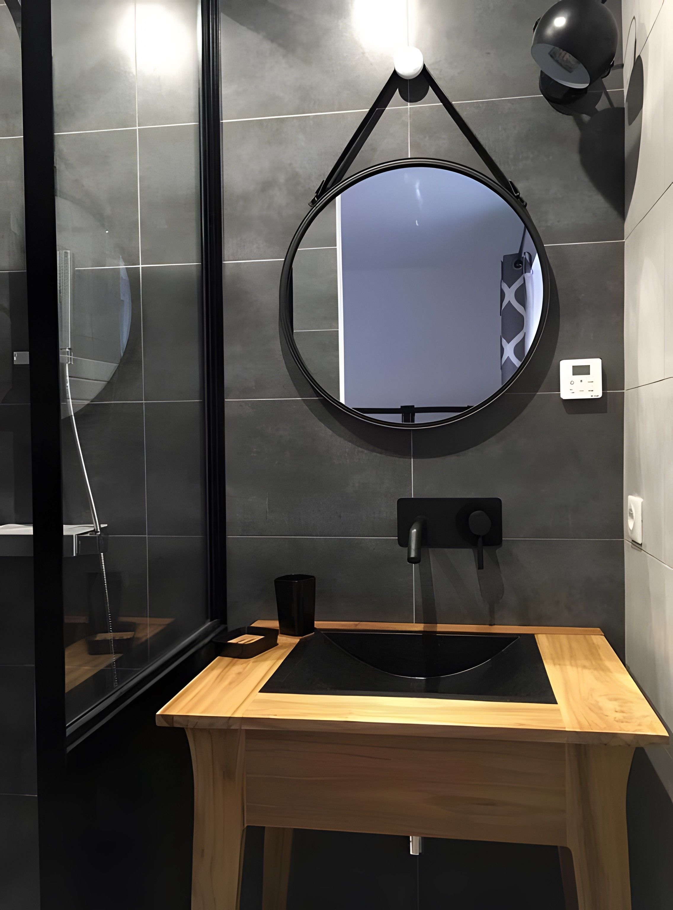 Une salle de bain moderne avec un lavabo noir, un miroir rond et un meuble-lavabo en bois.