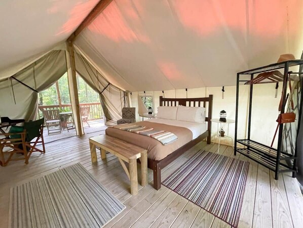 A tented accommodation with a single bed, wooden furniture, and a small table.