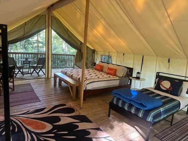 A tented accommodation with a bed, a bench, and a table.