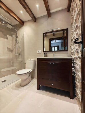 Une salle de bain moderne avec une douche à l’italienne en verre, des toilettes blanches et un meuble-lavabo en bois foncé agrémenté d’un mur d’accent en pierre.