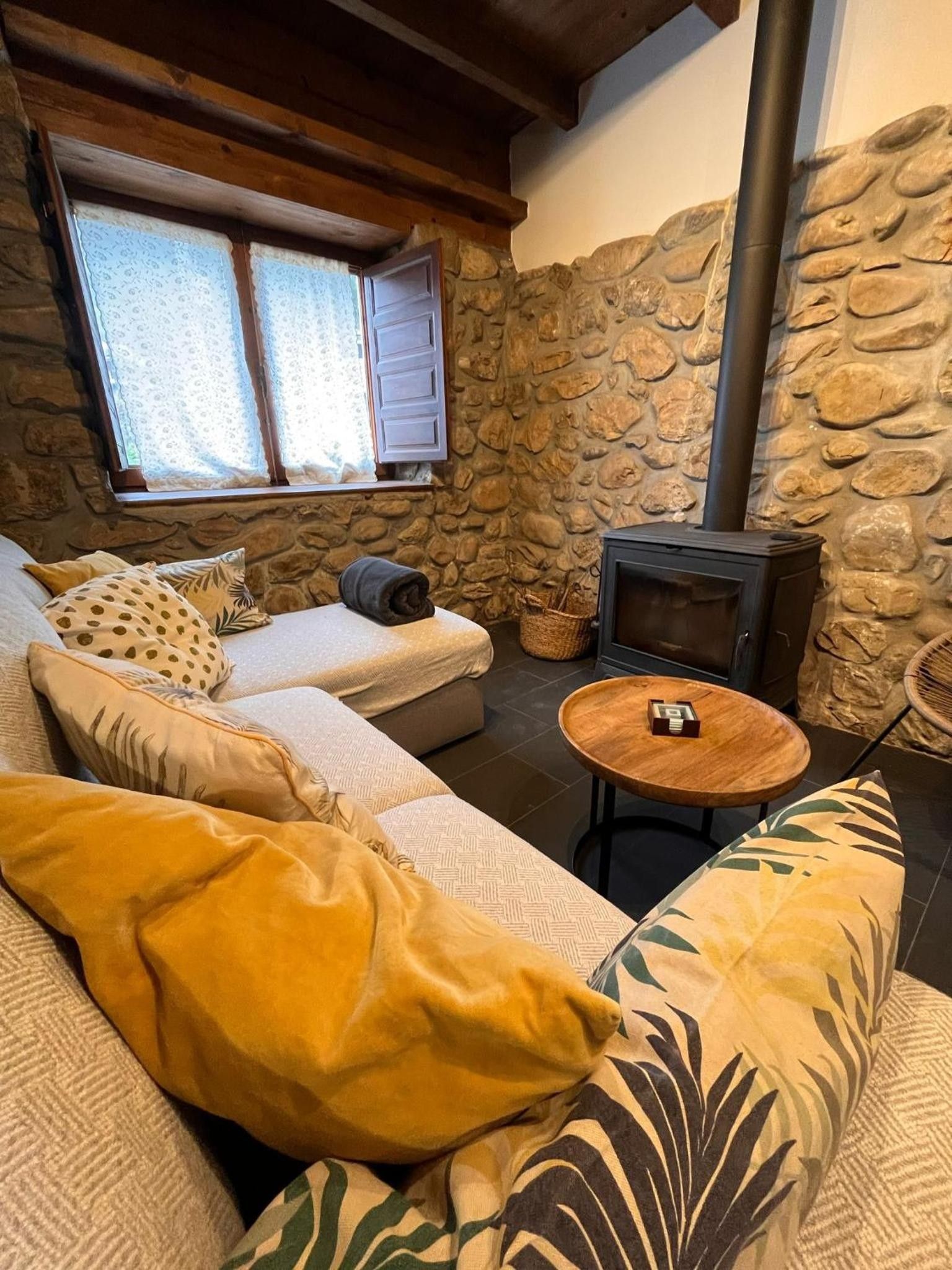 Un salon chaleureux avec un mur en pierre, un canapé agrémenté de coussins à motifs, une petite table en bois et une cheminée.