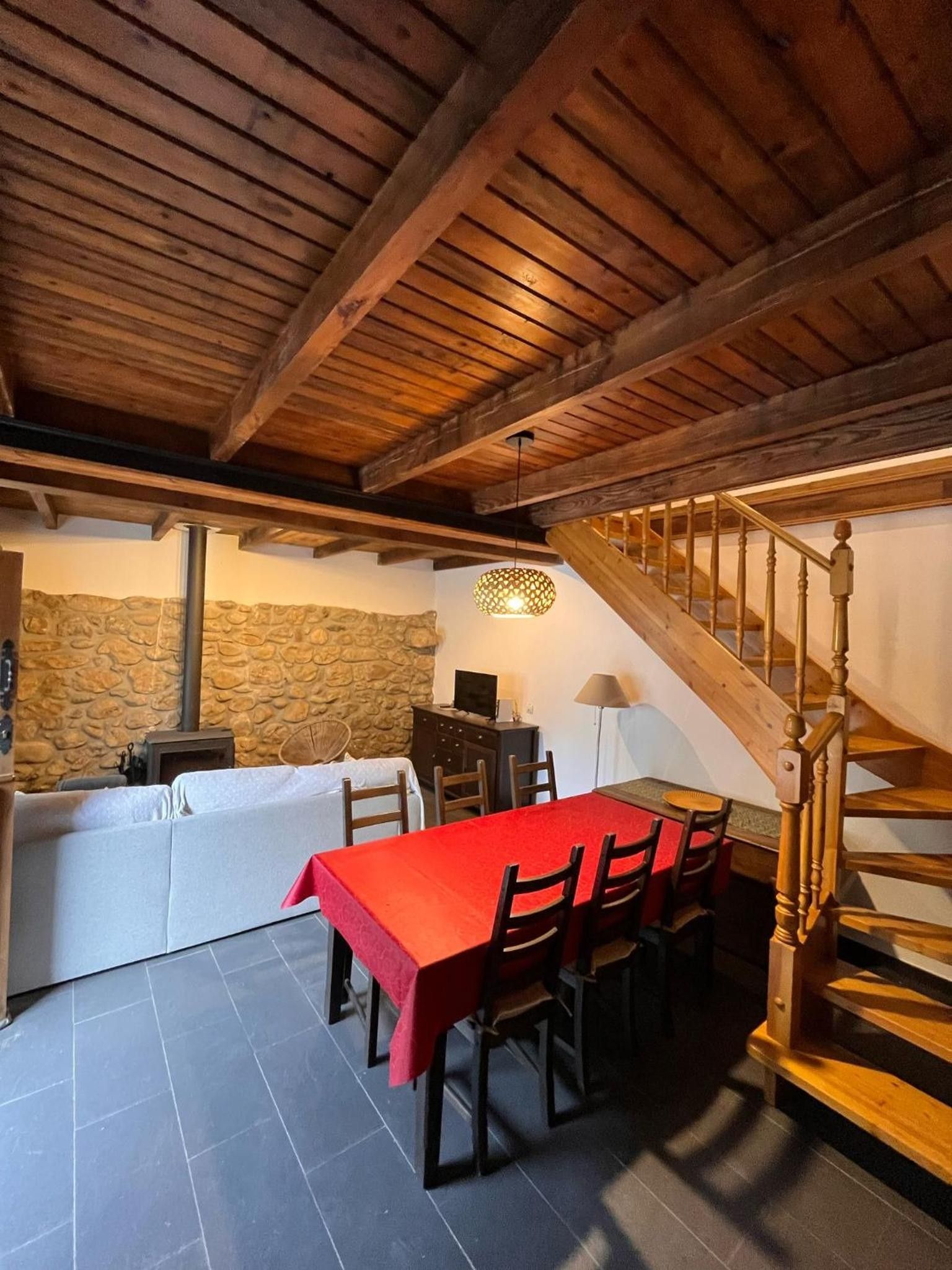 Un coin repas avec une table et des chaises rouges, un mur en pierre, une cheminée et un escalier en bois.