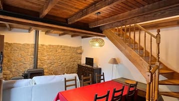 Un coin repas avec une table et des chaises rouges, un mur en pierre, une cheminée et un escalier en bois.