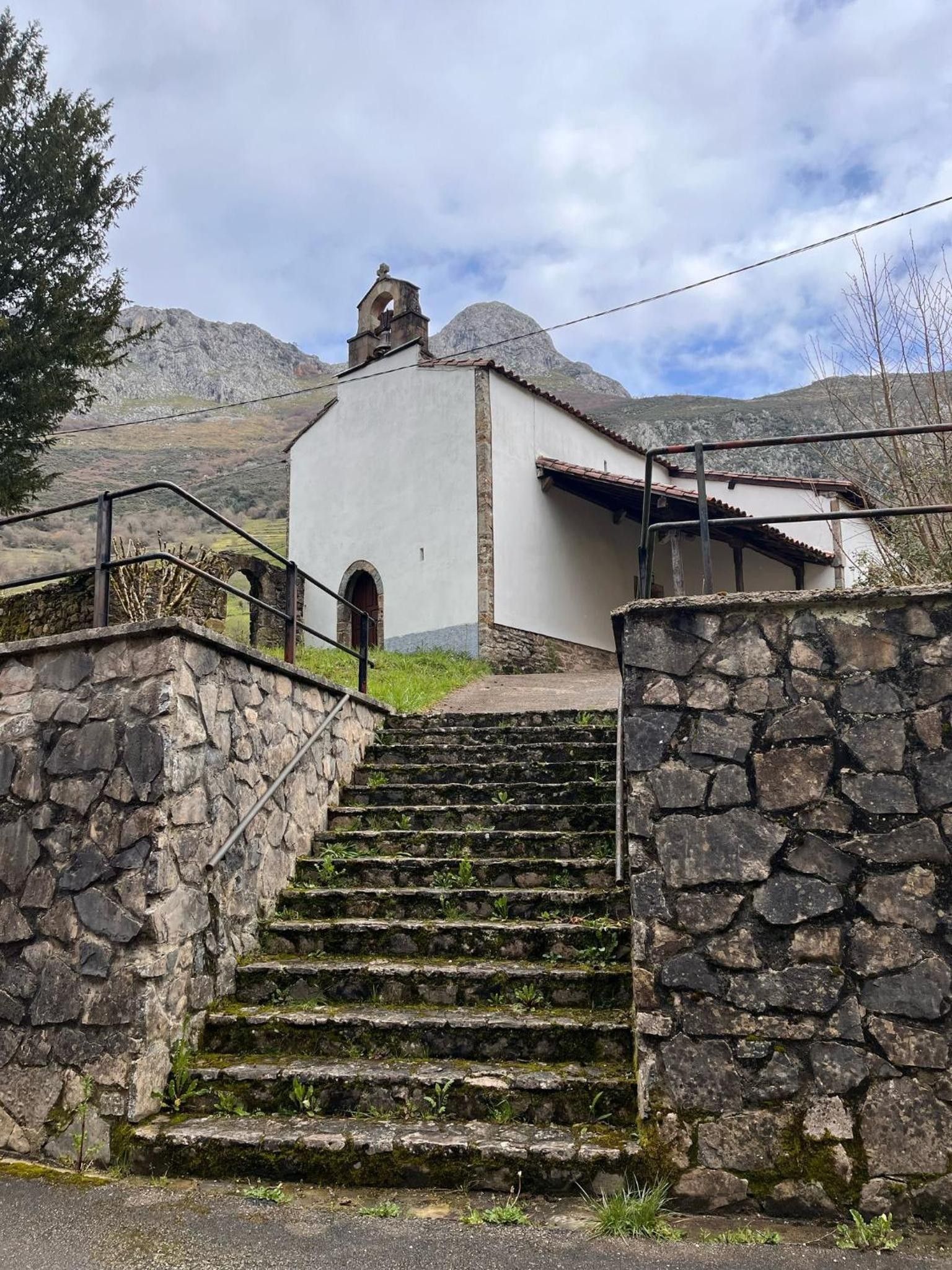 Un escalier en pierre mène à un bâtiment blanc surmonté d’un clocher, le tout étant entouré de montagnes.