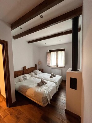 Une chambre avec deux lits, des poutres en bois au plafond, un radiateur et une fenêtre avec des rideaux.