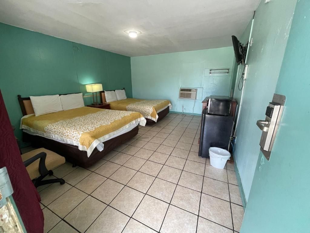 A room with two beds, a desk, a chair, a television, and a refrigerator.
