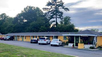 A motel with a row of parked cars, a single-story building, and a large tree in the background.