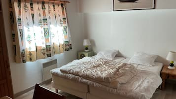 Une chambre à coucher avec un lit, des tables de chevet, une chaise, une fenêtre avec des rideaux et un tableau encadré au mur.