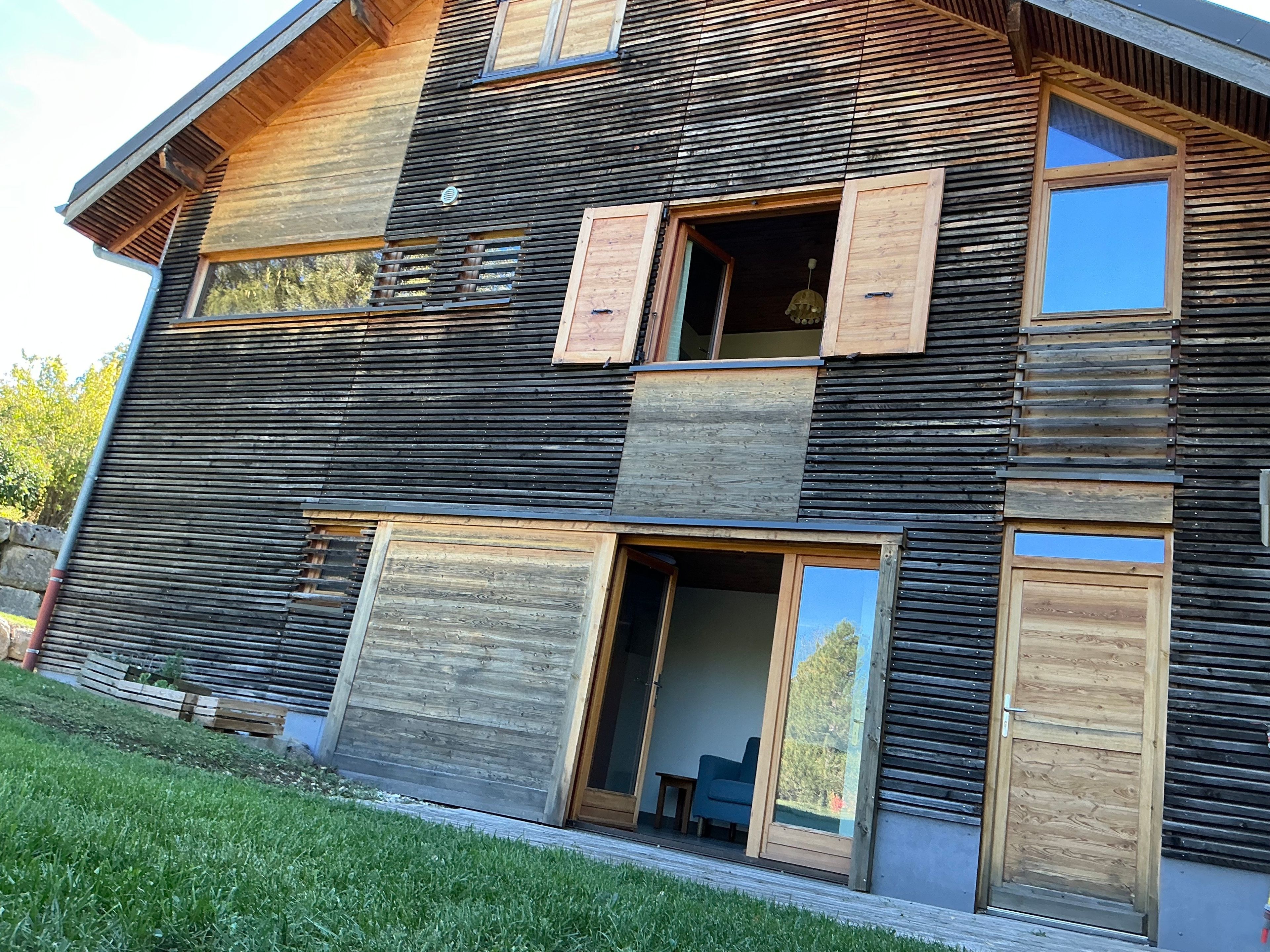 Un immeuble à plusieurs étages, doté d’un toit en pente, de grandes fenêtres et de volets en bois.
