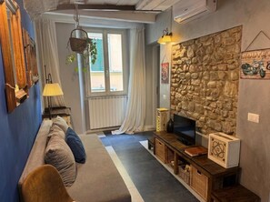 Un salon avec un mur en pierre, un canapé, un téléviseur et une fenêtre avec des rideaux.