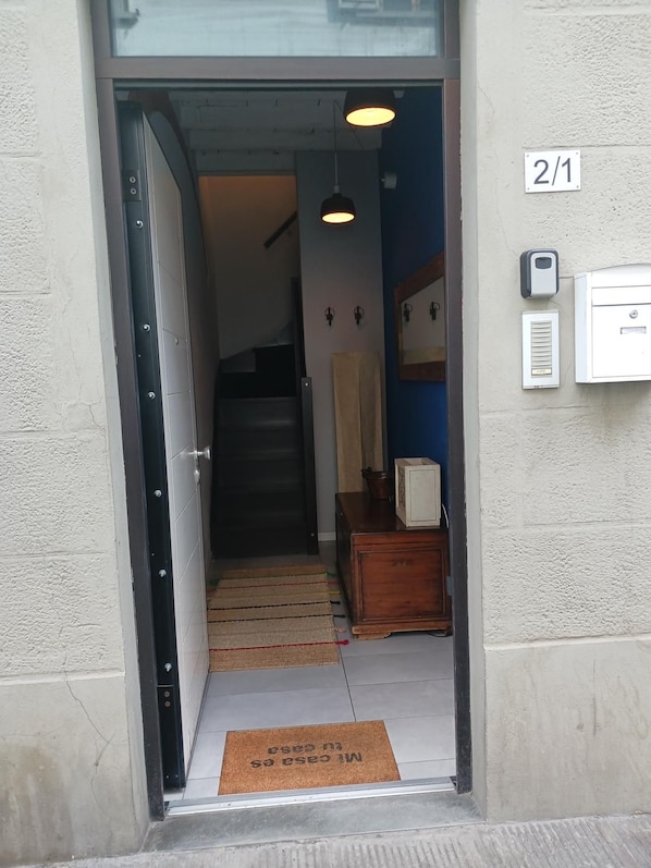 Une entrée avec un paillasson, un escalier et une boîte électrique fixée au mur.