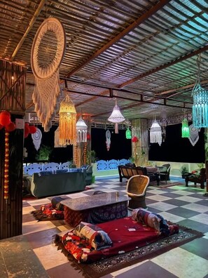 Uma área externa com assentos, piso xadrez, cadeiras de lounge e luminárias decorativas penduradas.