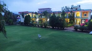Hotel com gramado bem cuidado, céu claro e edifício tradicional com vários andares e varandas.