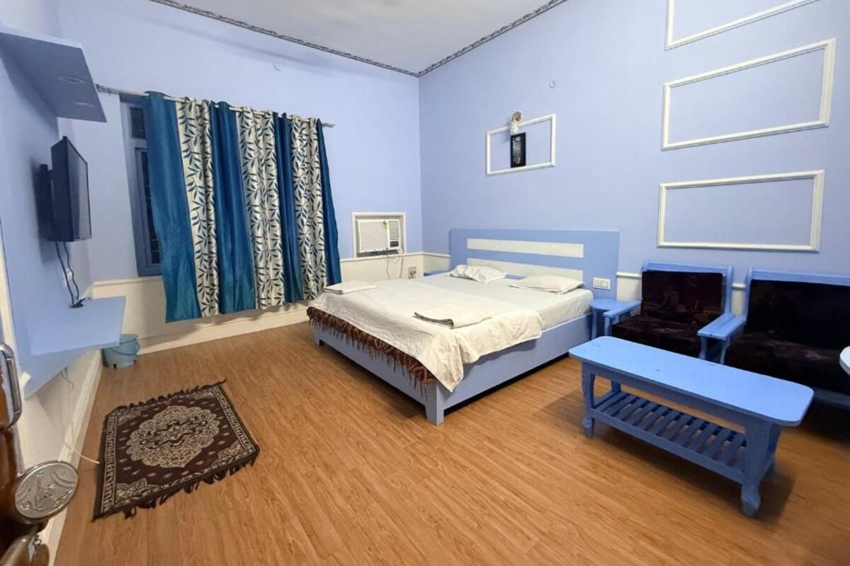 Quarto com cama, mesa de cabeceira, cadeira, televisão e janela com cortinas.