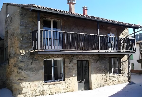 A two-story building with a balcony, a chimney, and a window with bars. - Country House 'Casa Rural Valdecorneja' with Private Terrace (Hoyorredondo)