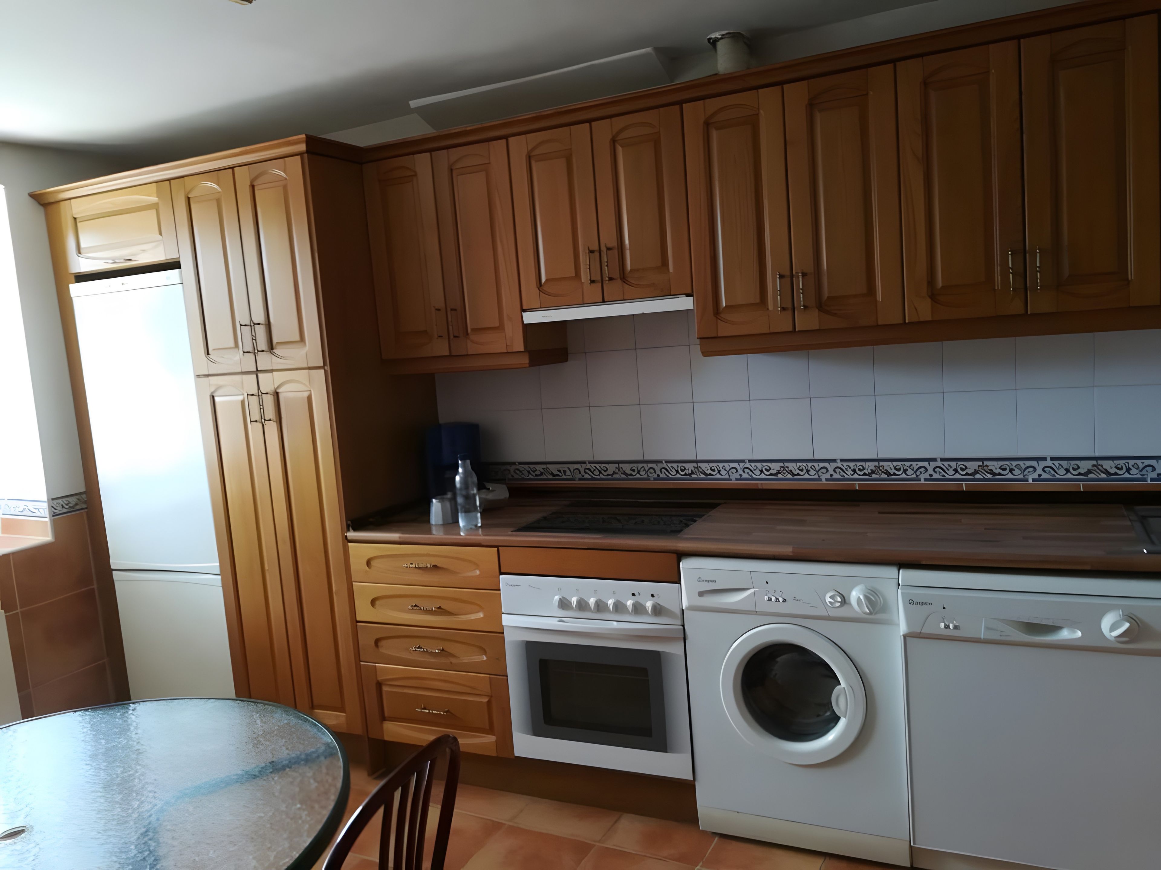A kitchen with wooden cabinets, a built-in oven, a washing machine, and a tiled backsplash.