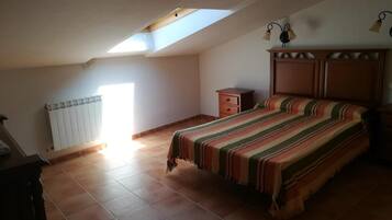 A bedroom with a sloped ceiling, a bed with a striped bedspread, a wooden dresser, and a radiator.