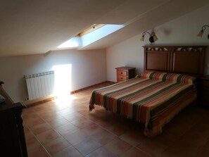 A bedroom with a sloped ceiling, a bed with a striped bedspread, a wooden dresser, and a radiator. - Country House 'Casa Rural Valdecorneja' with Private Terrace (Hoyorredondo)