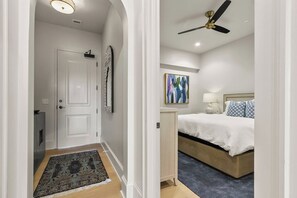 A hotel room with a bed, bedside table, lamp, and a ceiling fan. - Crimson Waters at Hill House | Golf Cart Optional (Tuscaloosa)