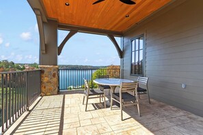 A covered patio with a table and chairs, a stone wall, and a view of the landscape. - The Retreat at Hill House (Tuscaloosa)
