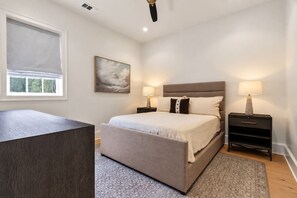 A bedroom with a bed, bedside tables, a window with blinds, a painting on the wall, and a rug on the floor. - The Retreat at Hill House (Tuscaloosa)