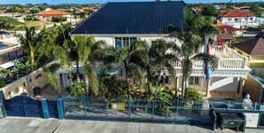 Un grand bâtiment doté d’un toit bleu foncé, entouré de palmiers et d’une clôture bleue.