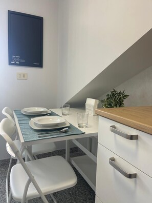 Un'area ristorazione con un tavolo apparecchiato per due, una sedia, una piccola pianta in vaso e un cartello con la scritta 'ROMA È DOVE SONO'.
