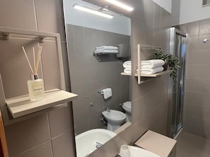 Un bagno moderno con vasca, servizi igienici e lavandino. Sono presenti mensole con asciugamani e una pianta.