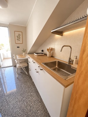 Una cucina moderna con lavello in acciaio inox, piano di lavoro in legno e mobili bianchi.
