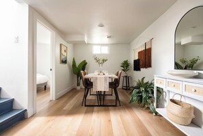 Et moderne spiseområde med trægulv, et spisebord dækket til fire personer og et stort spejl over vasken.