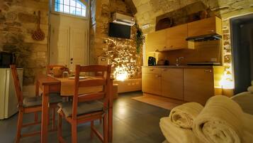 Una habitación acogedora con pared de piedra, una mesa de madera con sillas, una pequeña cocina y una ventana.
