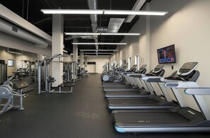 Une salle de sport équipée de tapis de course, d’appareils de musculation et d’un écran de télévision fixé au mur.