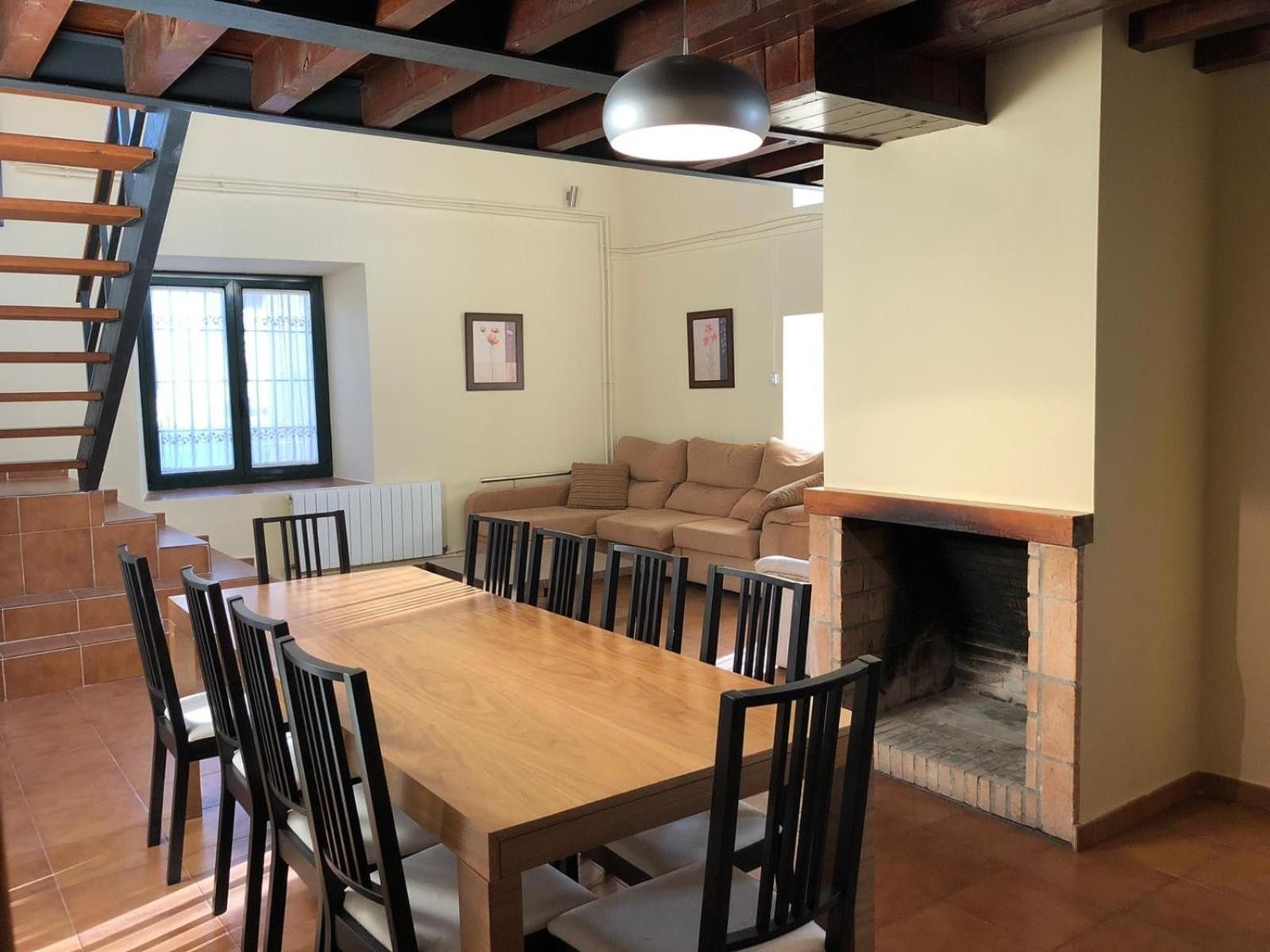Un espace repas comprenant une table et des chaises en bois, une cheminée, un canapé et un escalier.