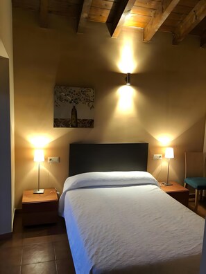 Une chambre à coucher avec un lit, deux tables de chevet, deux lampes fixées au mur, un tableau accroché au mur et un plafond en bois.