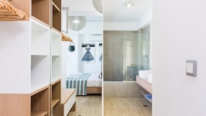 Une chambre à coucher moderne avec une armoire en bois, un lit avec une literie à rayures et une salle de bain dotée d’une cabine de douche en verre.