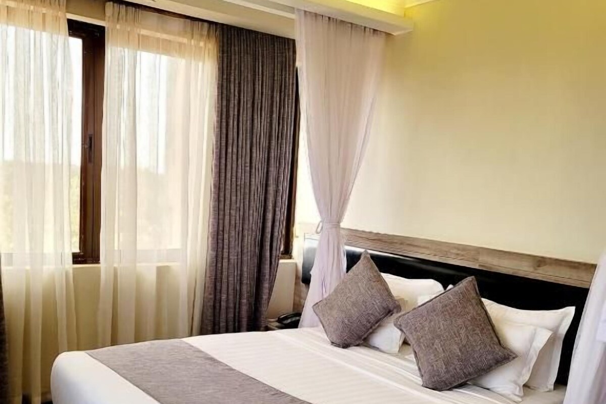 Hotellihuone, jossa on suuri sänky, verhot ja puulattia.