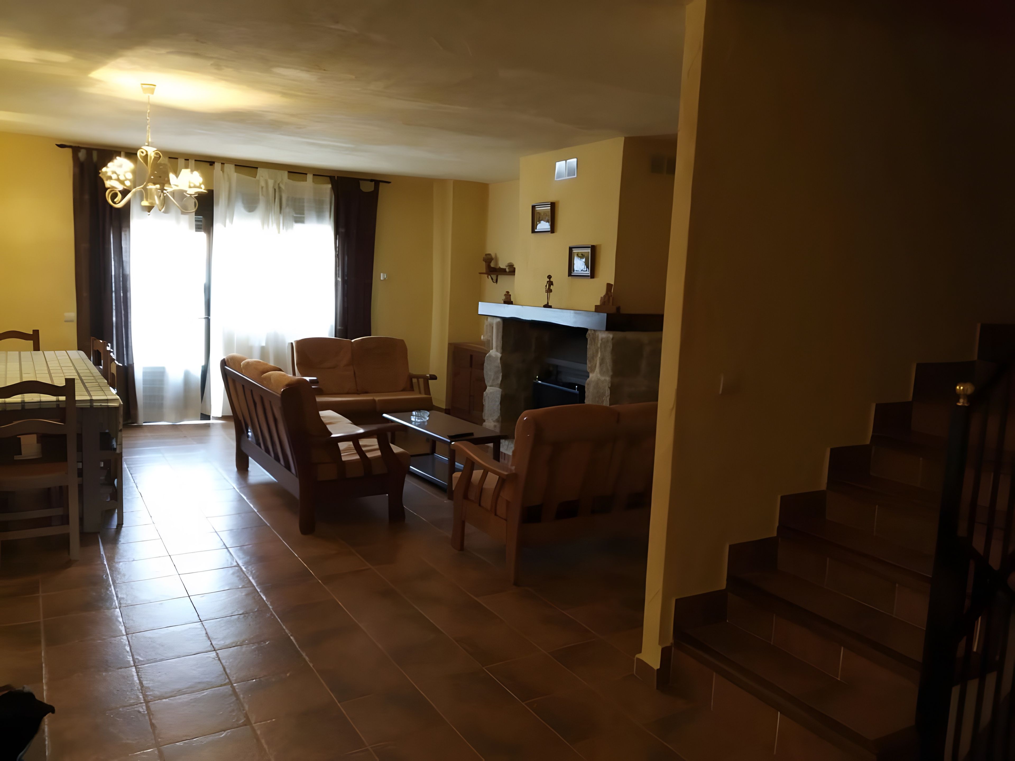 Una sala de estar con chimenea, un comedor con mesa y sillas, y una escalera que sube a otro nivel.