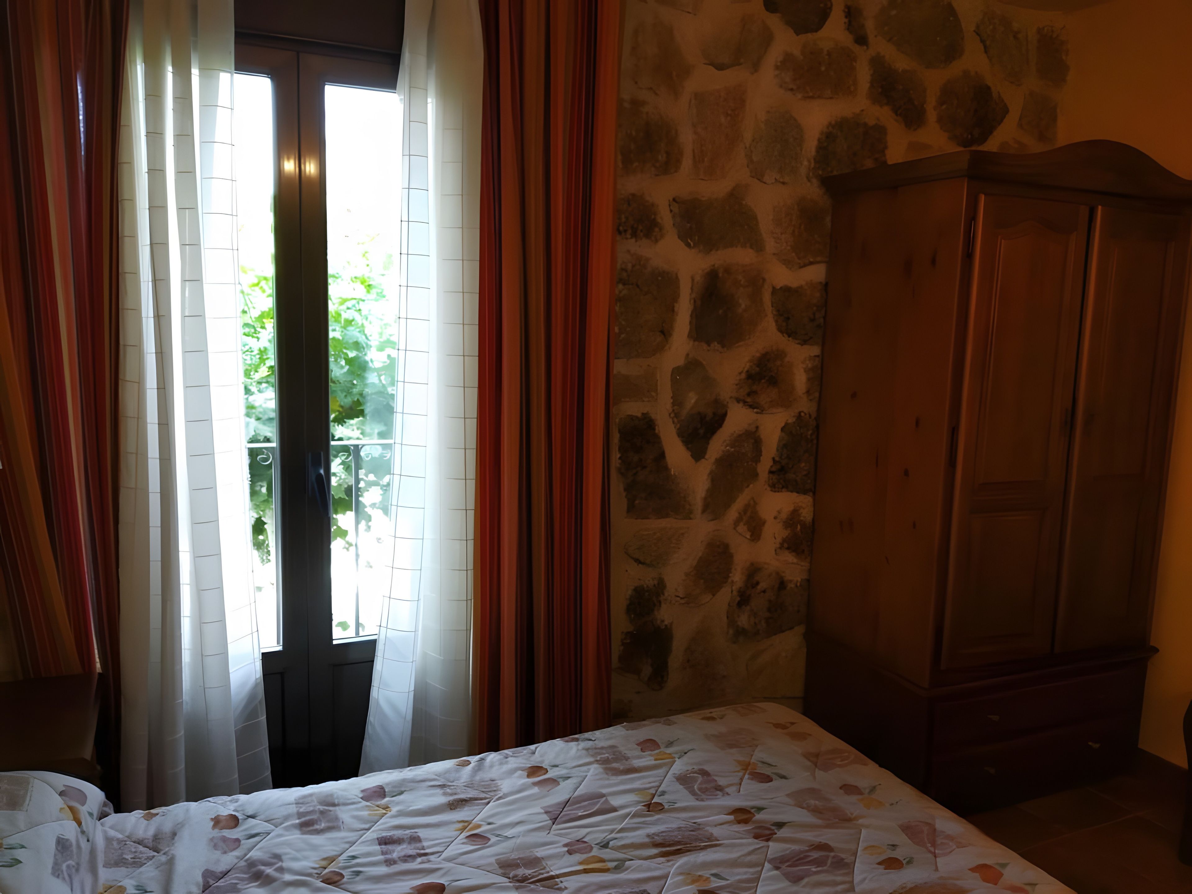 Una habitación con una cama, un armario de madera y una pared de piedra.