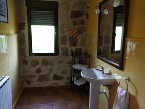 Un baño con pared de piedra, una ventana, un lavabo y un espejo.