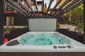 Een hottub met een houten terras en een gebouw op de achtergrond.