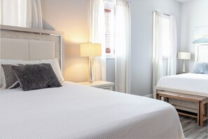 Una habitación de hotel con dos camas, una mesita de noche con lámpara y una ventana con cortinas.