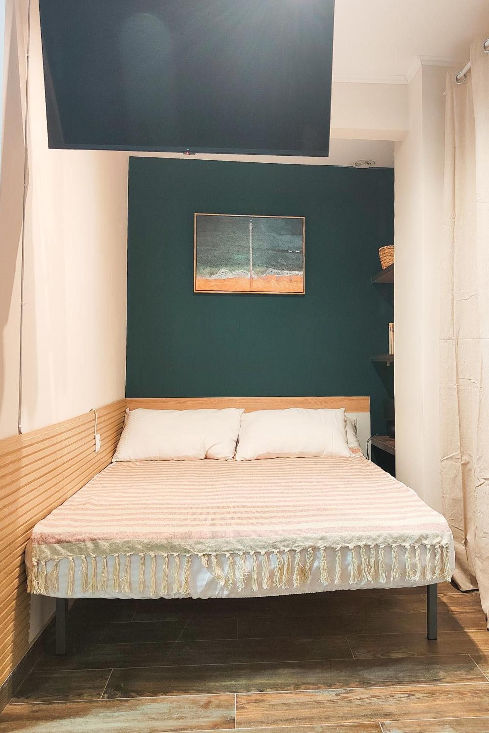 Ein Zimmer mit einem Bett, einer dunkelgrünen Wand, einem gerahmten Bild und einem Holzkopfteil.