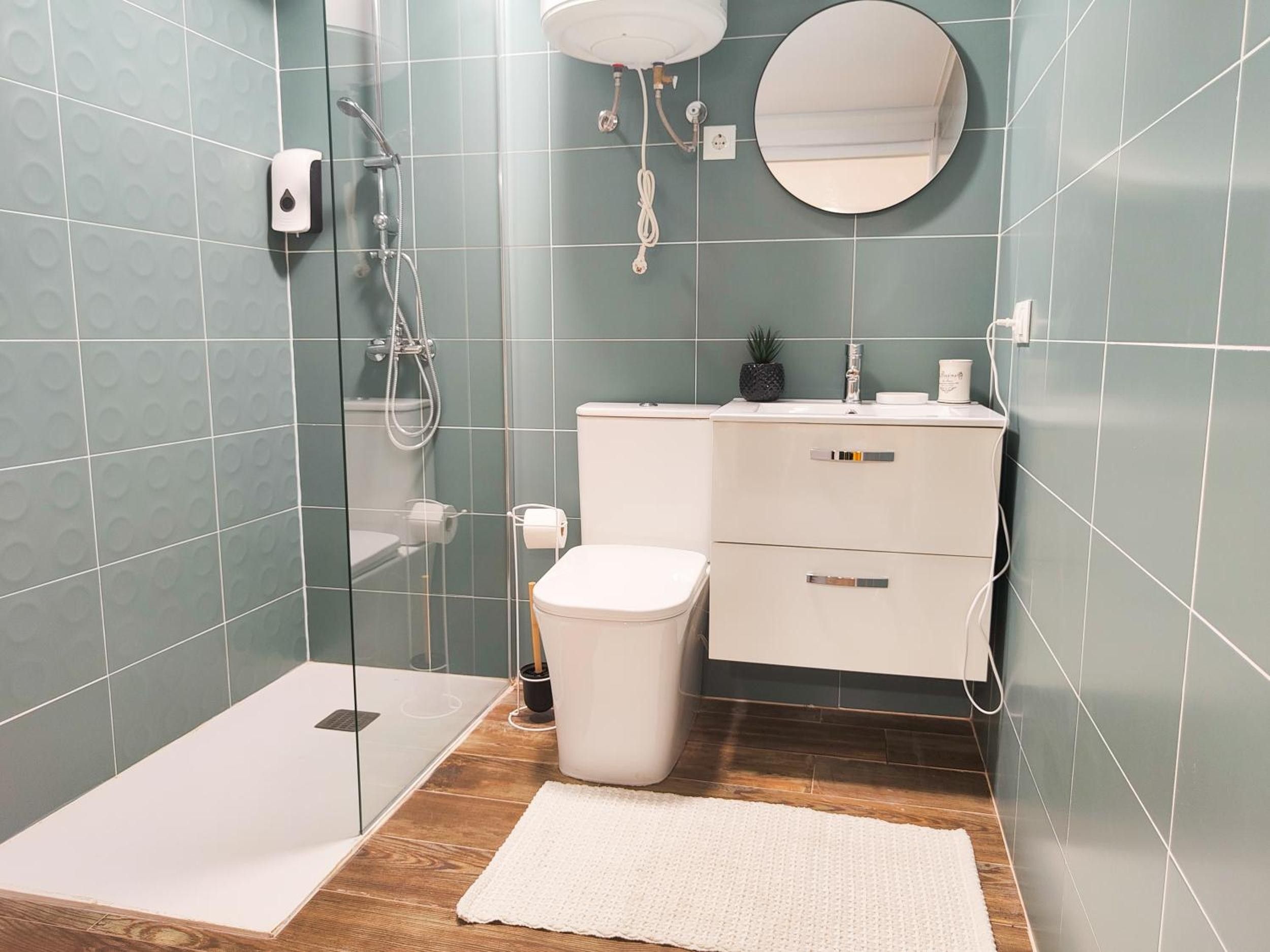 Ein Badezimmer mit Duschkabine aus Glas, einer weißen Toilette, einem Waschbecken mit Spiegel und einem Holzboden.