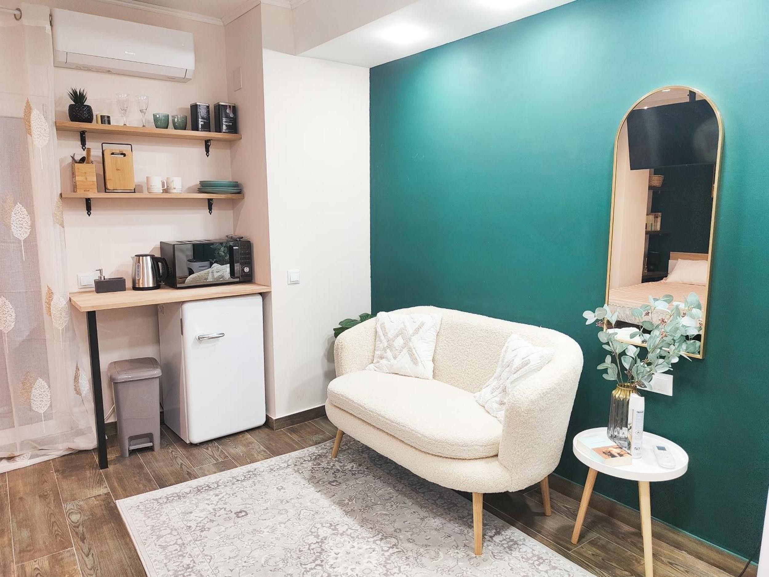 Ein gemütlicher Wohnraum mit Küchenzeile, einer Couch, einem kleinen Tisch mit Blumenvase und einem Spiegel an der Wand.