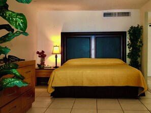 A hotel room with a bed, a nightstand, a lamp, a telephone, and a potted plant. - New Listing (Puerto Vallarta)